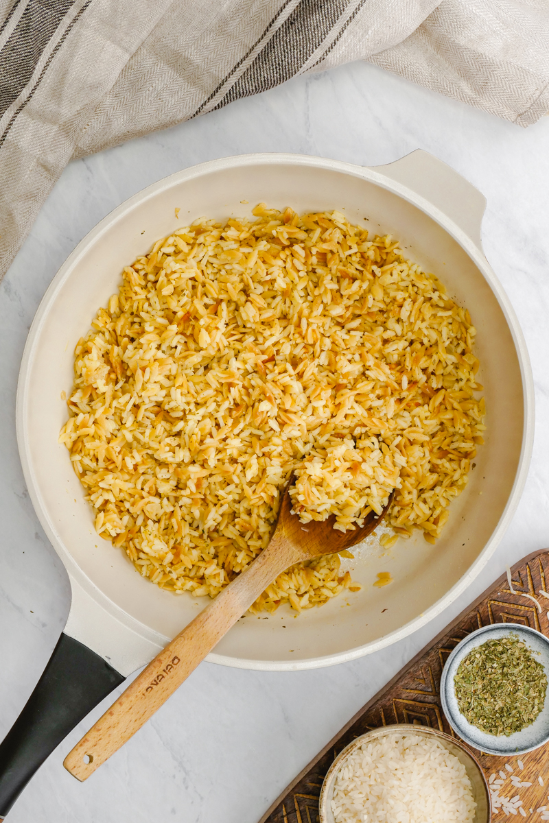 Cooking rice pilaf in a skillet stove top, with a wooden spoon scooping some of the rice pilaf