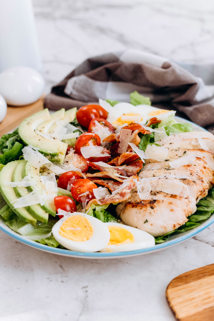 A plate of chicken avocado caesar salad, with a napkin behind and some boiled eggs