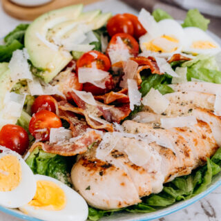 Chicken avocado caesar salad, a bed of lettuce topped with eggs, chicken, tomatoes, bacon, and avocados.