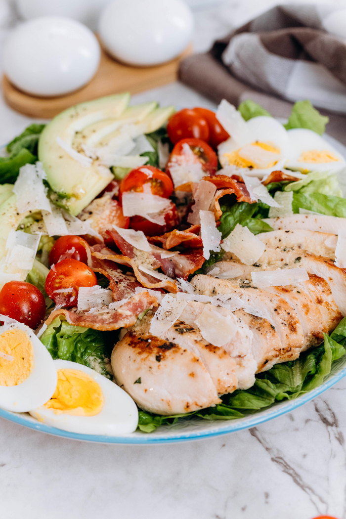 Chicken avocado caesar salad, a bed of lettuce topped with eggs, chicken, tomatoes, bacon, and avocados. 