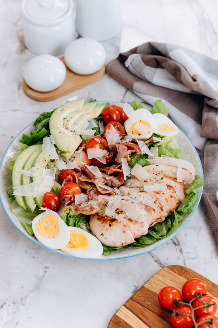 A chicken avocado caesar salad on a marble slab, and with salt and pepper shakers behind