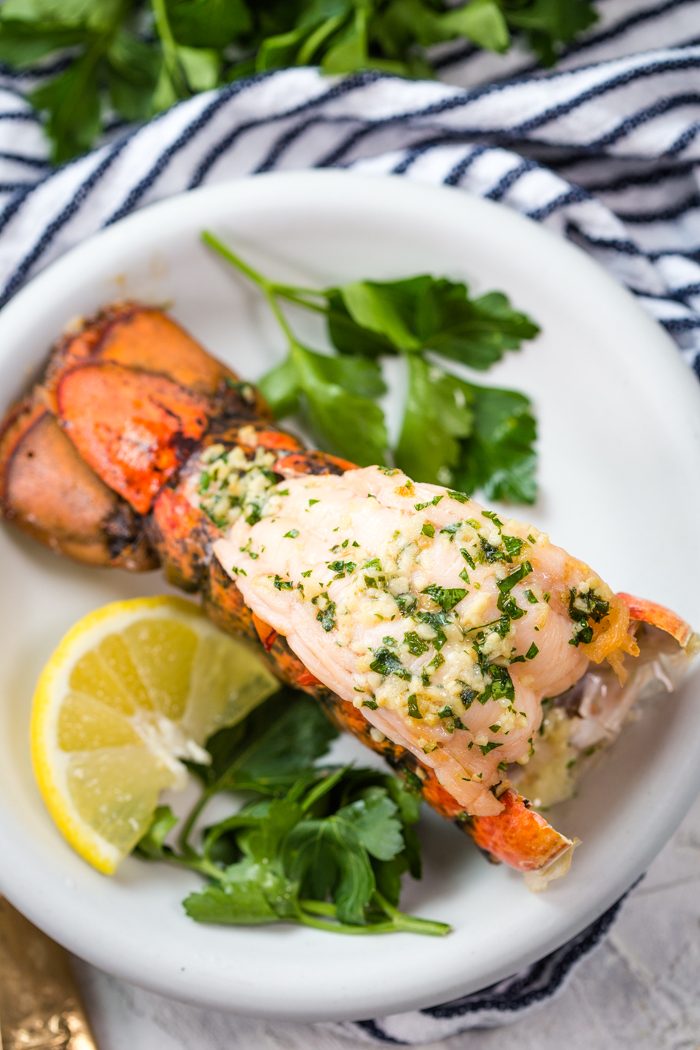 Broiled Lobster on a white plate with parsley and lemon wedge