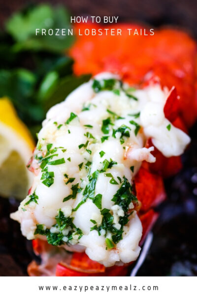 A cooked lobster tail covered with butter and garlic and parsley, next to a wedge of lemon