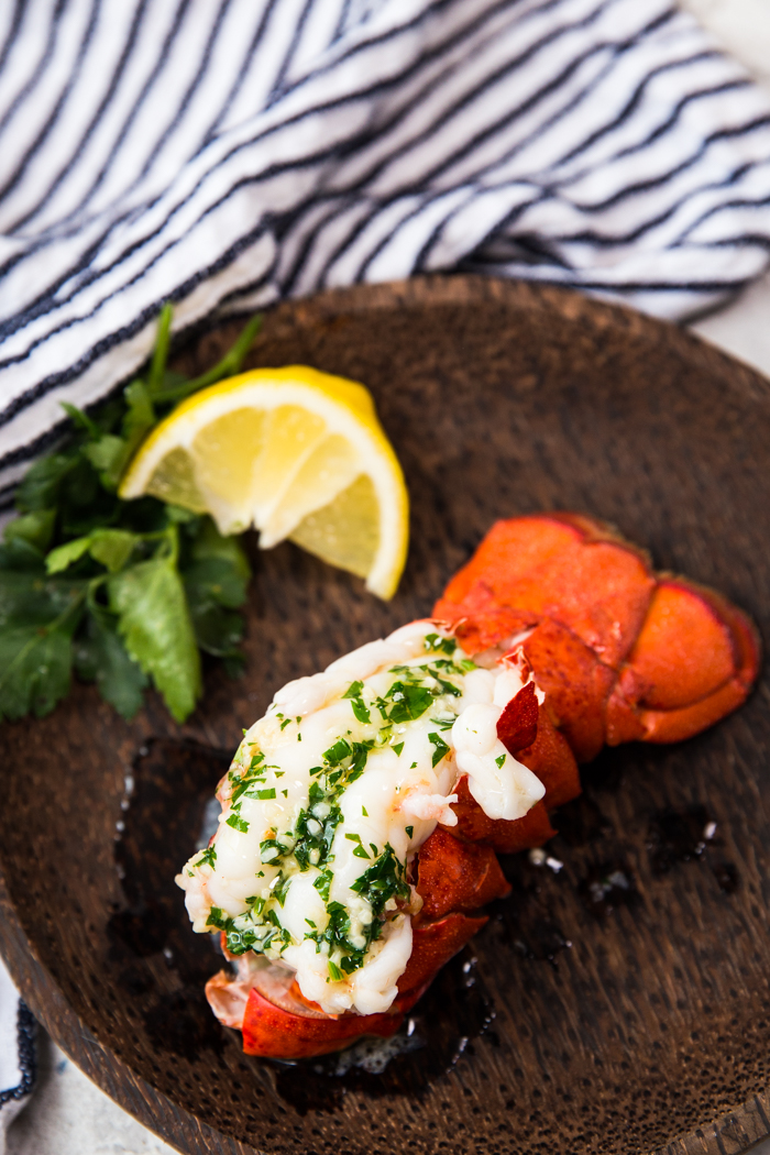 Steamed lobster tail on a wood plate with parsley and lemon wedges