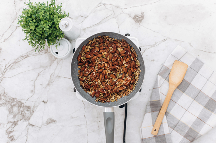 ingredients for keto granola all mixed up in pan with wood spatula