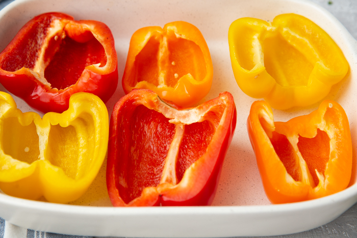 A baking pan with red, orange, and yellow pepper halves