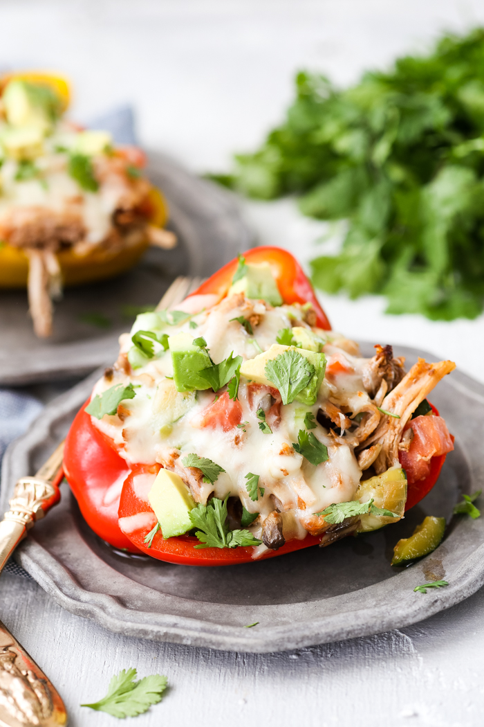 Pork stuffed pepper topped with mozzarella, cilantro, and avocado, on a pewter plate, with cilantro in the background