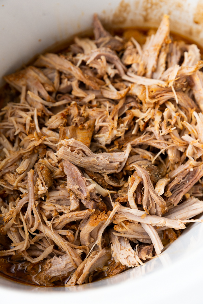 Sweet and Smoky roasted pork shredded and in a white crock pot