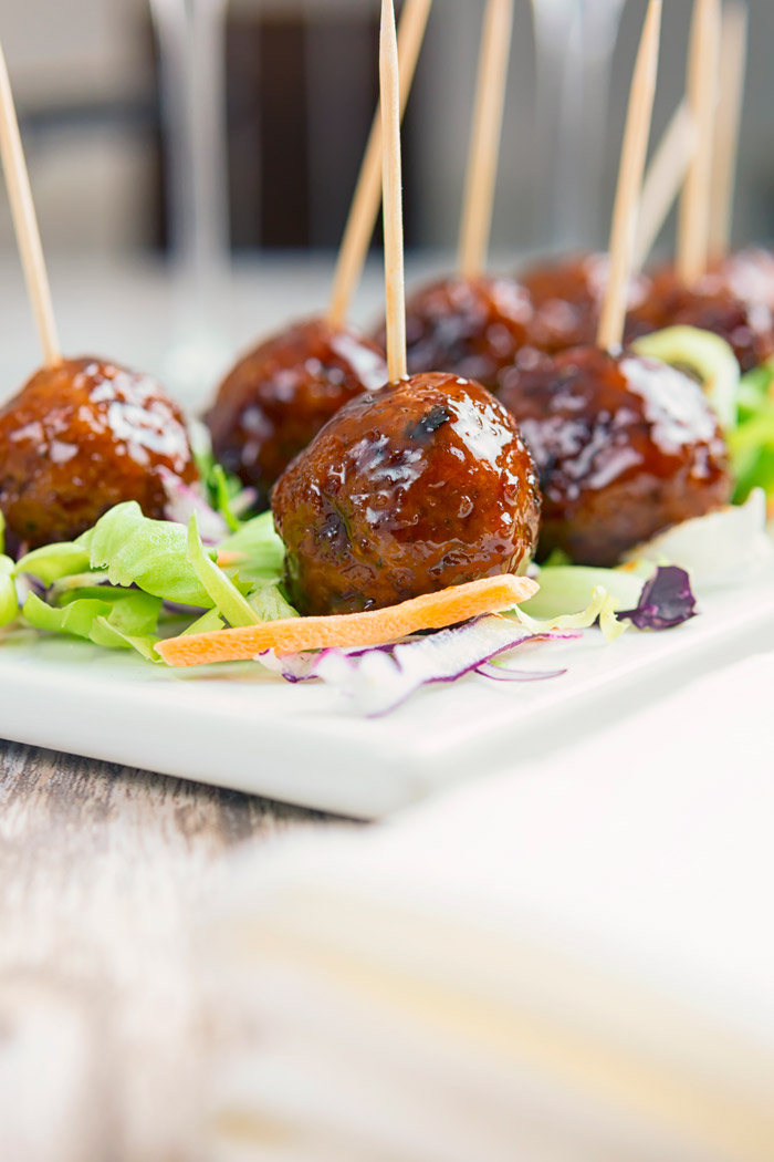 Delicious glazed meatballs on a serving tray atop a bed of greens. 