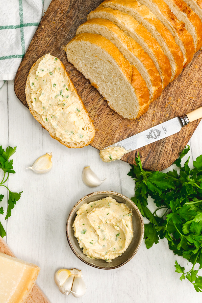 homemade garlic bread, a loaf of italian bread, a bowl of herbs and butter and garlic