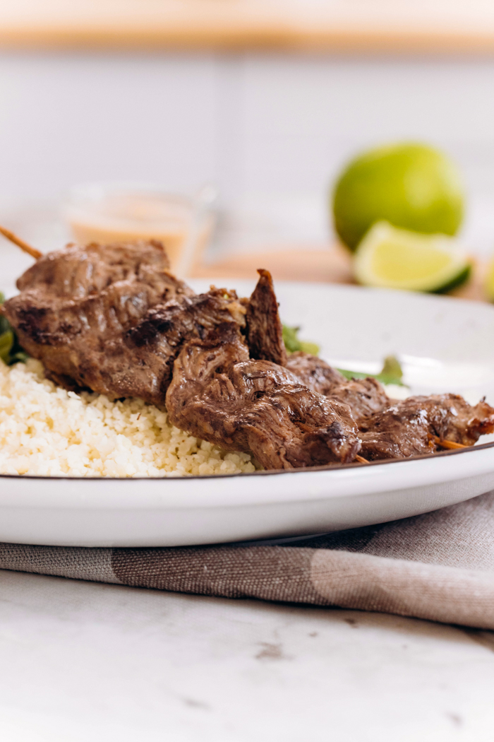 Low carb beef satay on a white plate with limes in the background