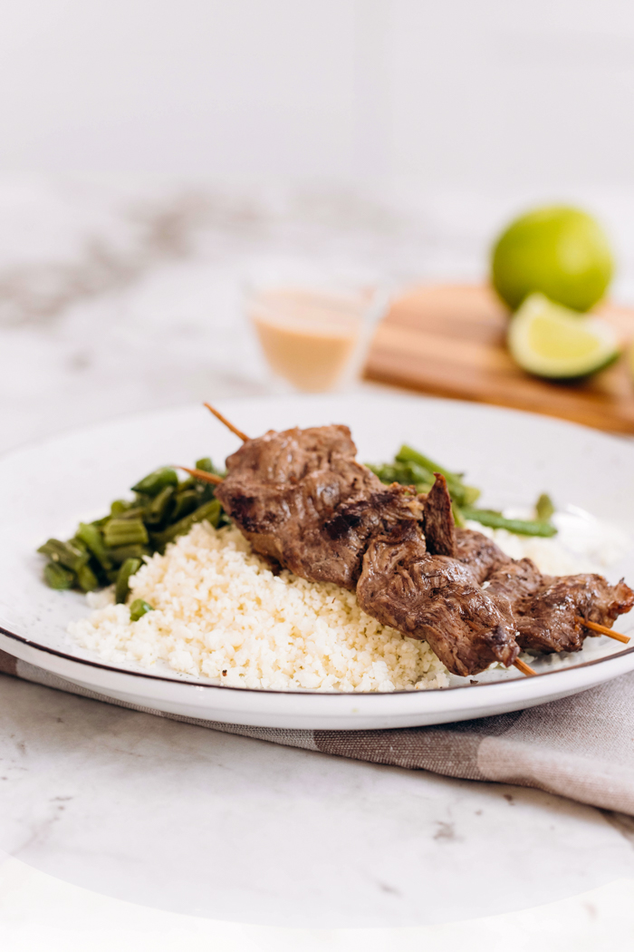 a plate with two skewers of beef satay with peanut sauce and limes