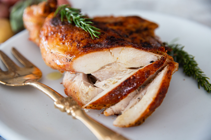 A white platter with a juicy air fryer turkey breast sliced, and garnished with rosemary