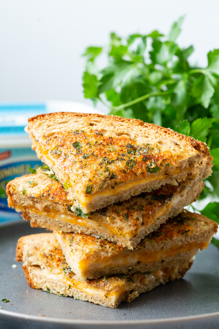 Garlic Parmesan Grilled Cheese sandwich cut into four pieces and stacked on a gray plate with parsley behind