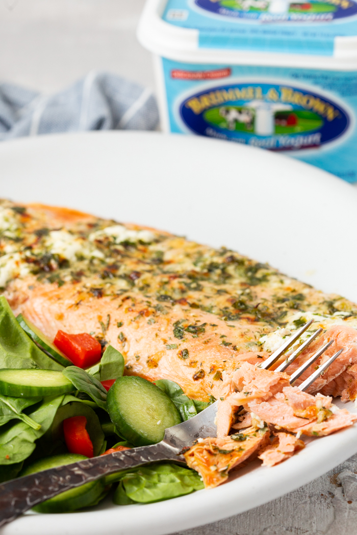 Oven baked salmon on a white plate with a spinach salad and a fork