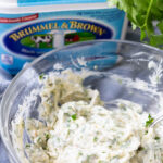 Garlic Parmesan Herb Spread in a clear glass bowl with parsley in the background
