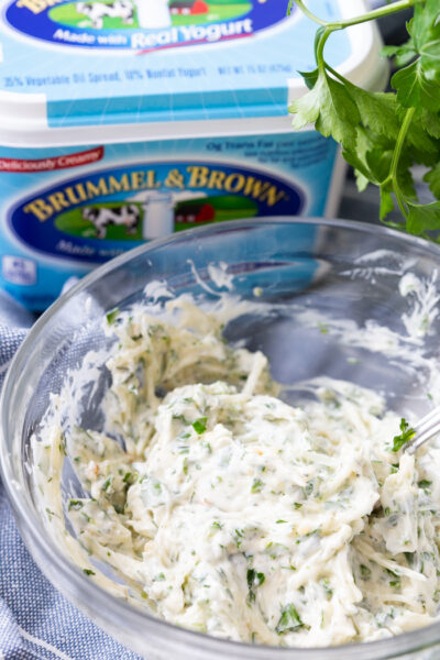 Garlic Parmesan Herb Spread in a clear glass bowl with parsley in the background