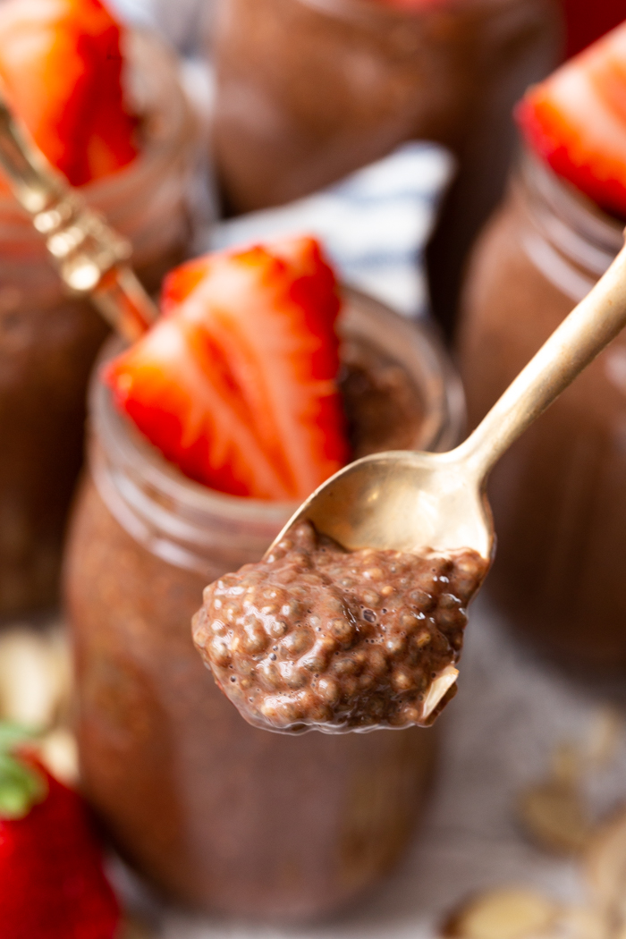 Chocolate almond chia pudding on a gold spoon with a jar in the background with strawberry slices