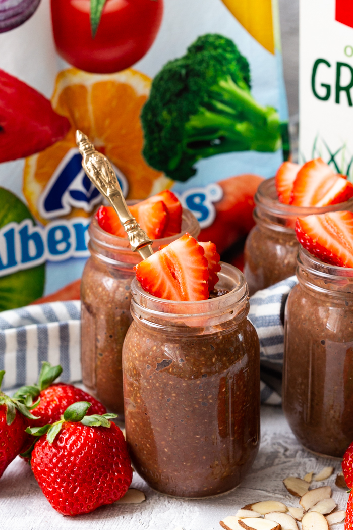 Chocolate almond chia pudding in glass jars with strawberries on top and an Albertsons bag behind. 