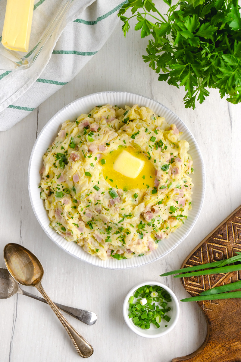 An overhead shot of a big bowl of irish colcannon with a pad of butter and parsley on top. 