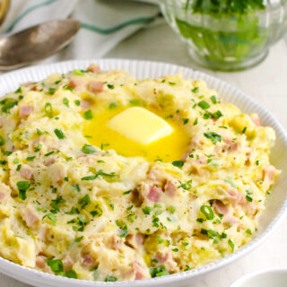 Colcannon in a white bowl with parsley and spoons in the background