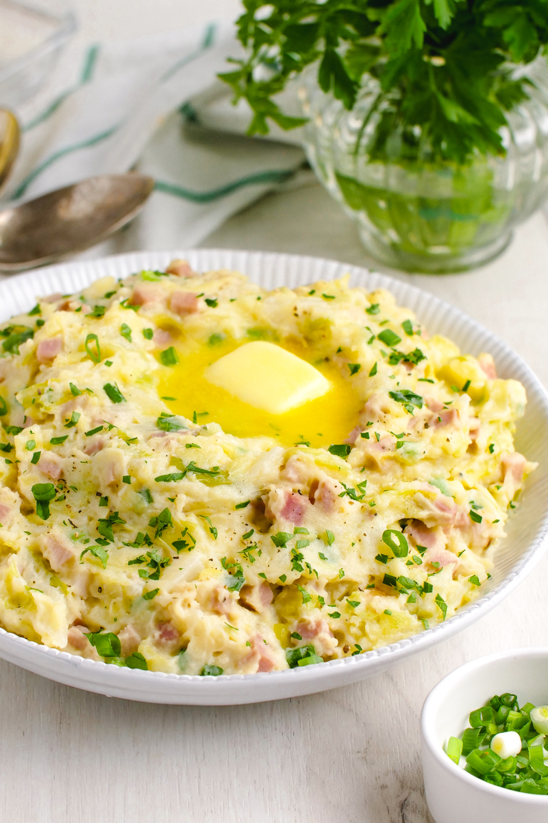 Colcannon in a white bowl with parsley and spoons in the background