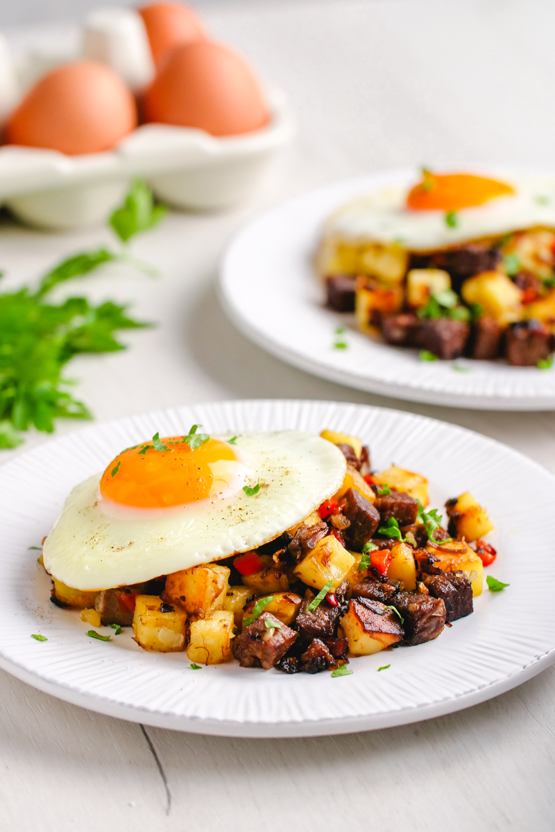 two plates topped with corned beef hash and an egg, garnished with parsley