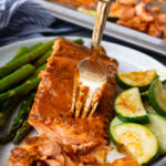 Cajun Butter baked salmon on a white plate with vegetables cooked on the same sheetpan