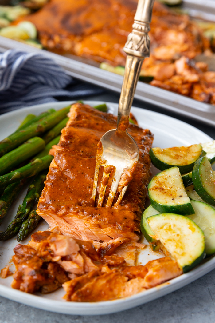 Cajun Butter baked salmon on a white plate with vegetables cooked on the same sheetpan