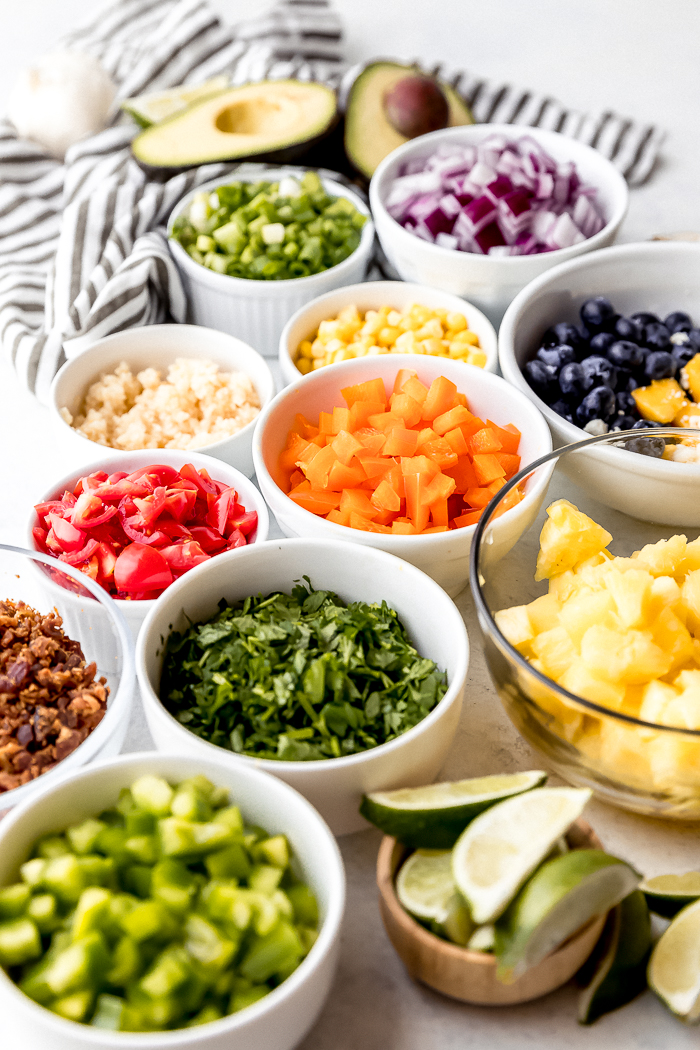 several bowls with chopped up ingredients for a guacamole bar