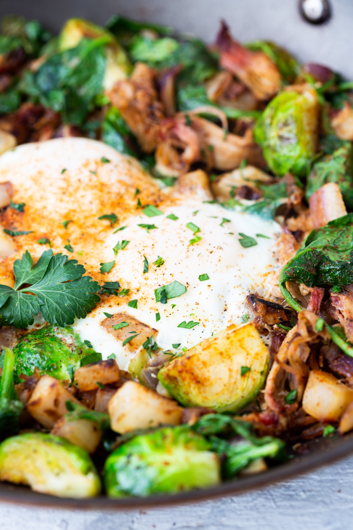 A close up of a pulled pork breakfast hash with eggs on top and garnish