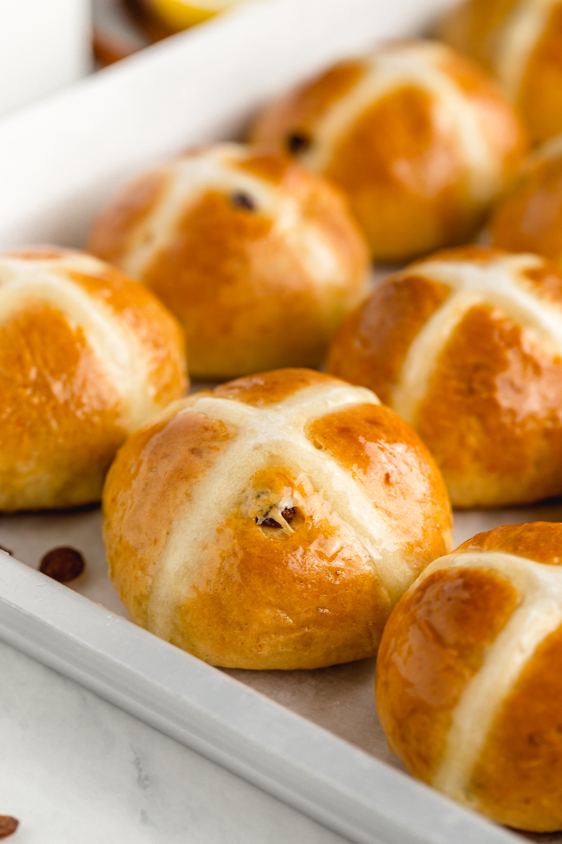 A close up of hot cross buns studded with rum soaked currants and glazed
