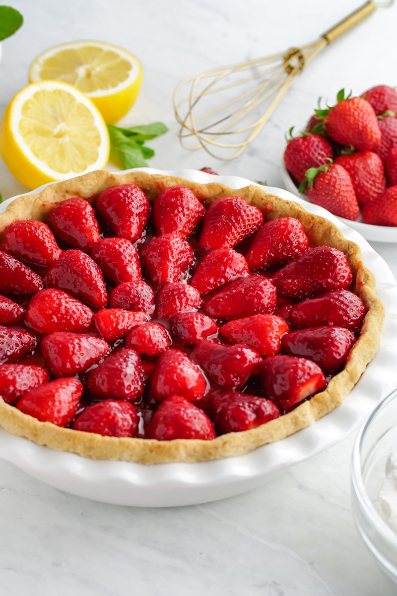 Fresh strawberry pie, a whole pie in a white pie plate with lemons and mint in the background