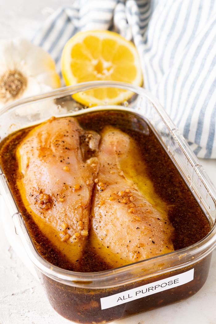 A container with two chicken breasts in it covered in an all purpose marinade