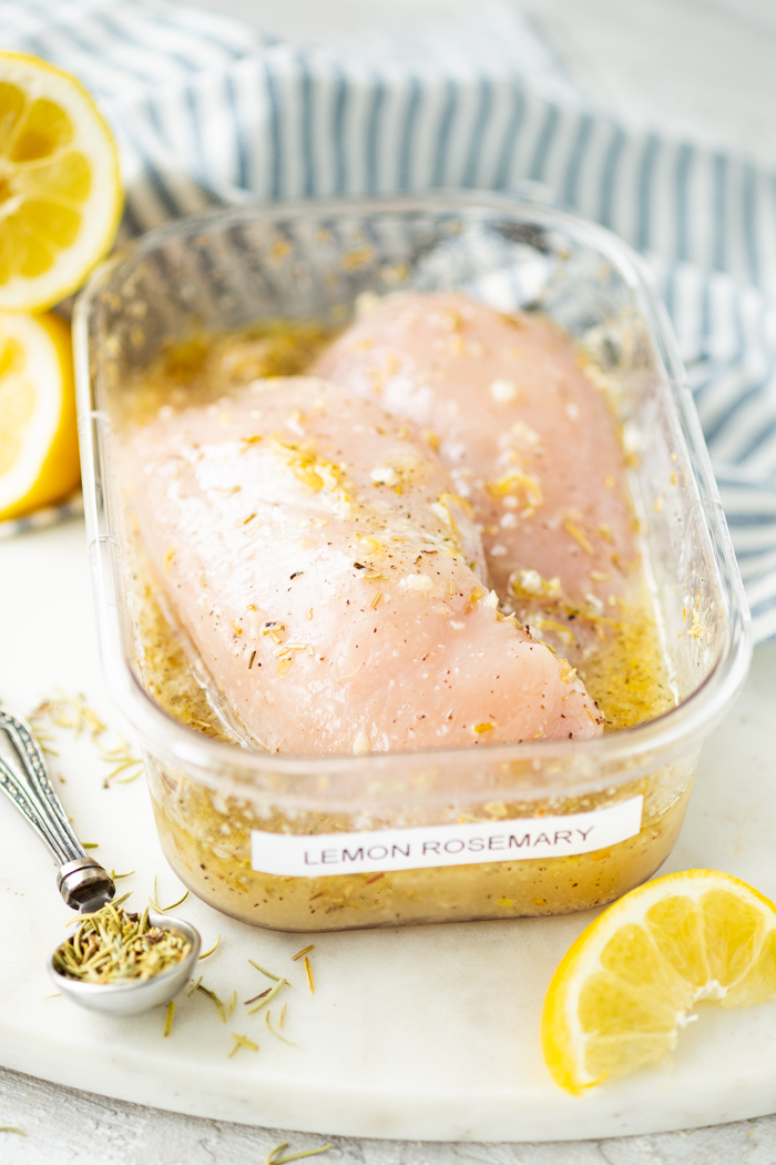 A container with two chicken breasts and lemon rosemary marinade