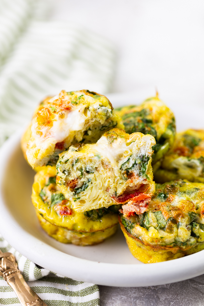 A white plate with egg muffins, one egg muffin is cut in half 