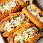 A top down shot of a tray of sloppy joe meatball subs with melted mozzarella cheese.