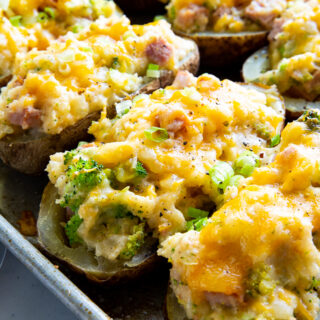 A sheet pan loaded with twice baked potatoes. Melted cheese on top, broccoli and ham pieces showing in the mashed potatoes.