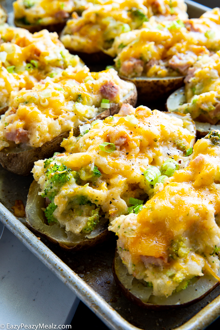 A sheet pan loaded with twice baked potatoes. Melted cheese on top, broccoli and ham pieces showing in the mashed potatoes.