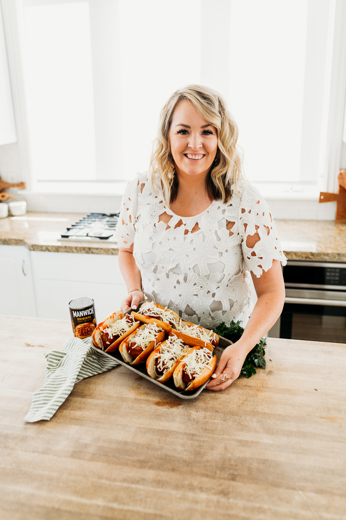 A woman holding a tray of manwich sloppy joe meatball subs.