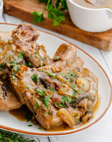 Smothered pork chops on a white serving dish with a cutting board and gravy in the background.