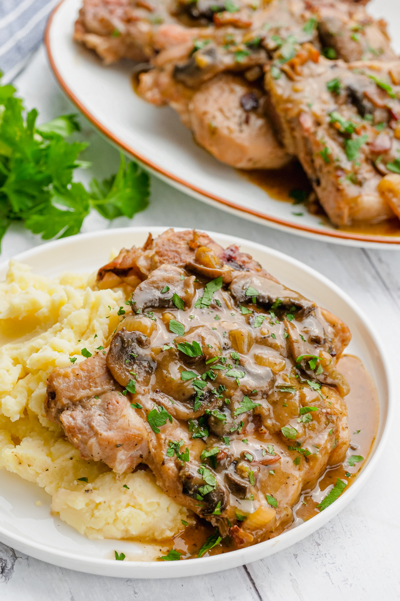 A white plate with mashed potatoes and a smothered pork chop