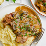 A smothered pork chop with mashed potatoes, on a white plate