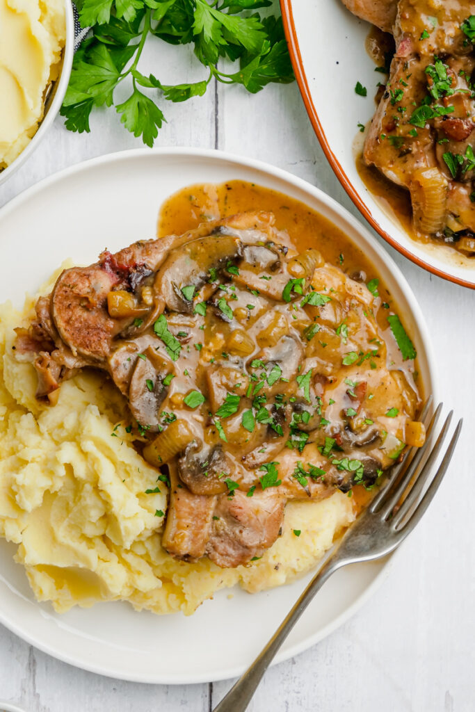 A smothered pork chop with mashed potatoes, on a white plate