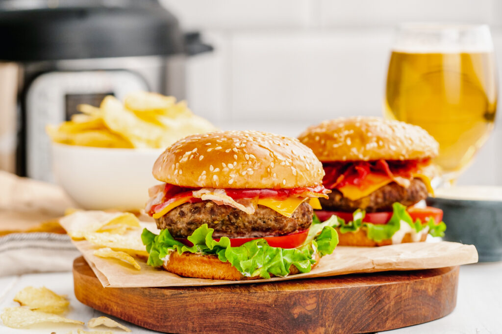 Two cheese stuffed hambugers with fries in the background, an instant pot, and a glass of beer. 