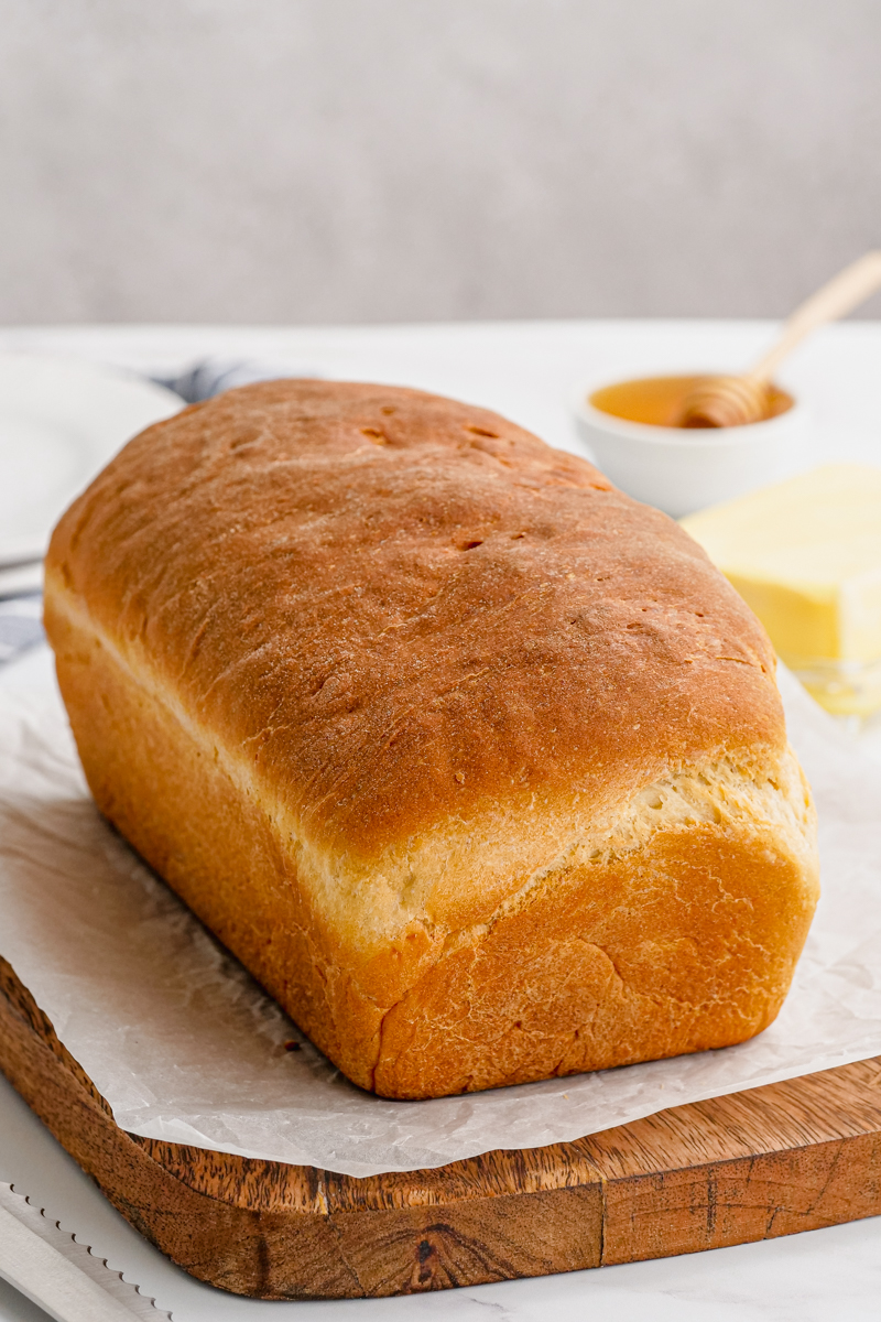 A loaf of baked sandwich bread on a wooden cutting board.