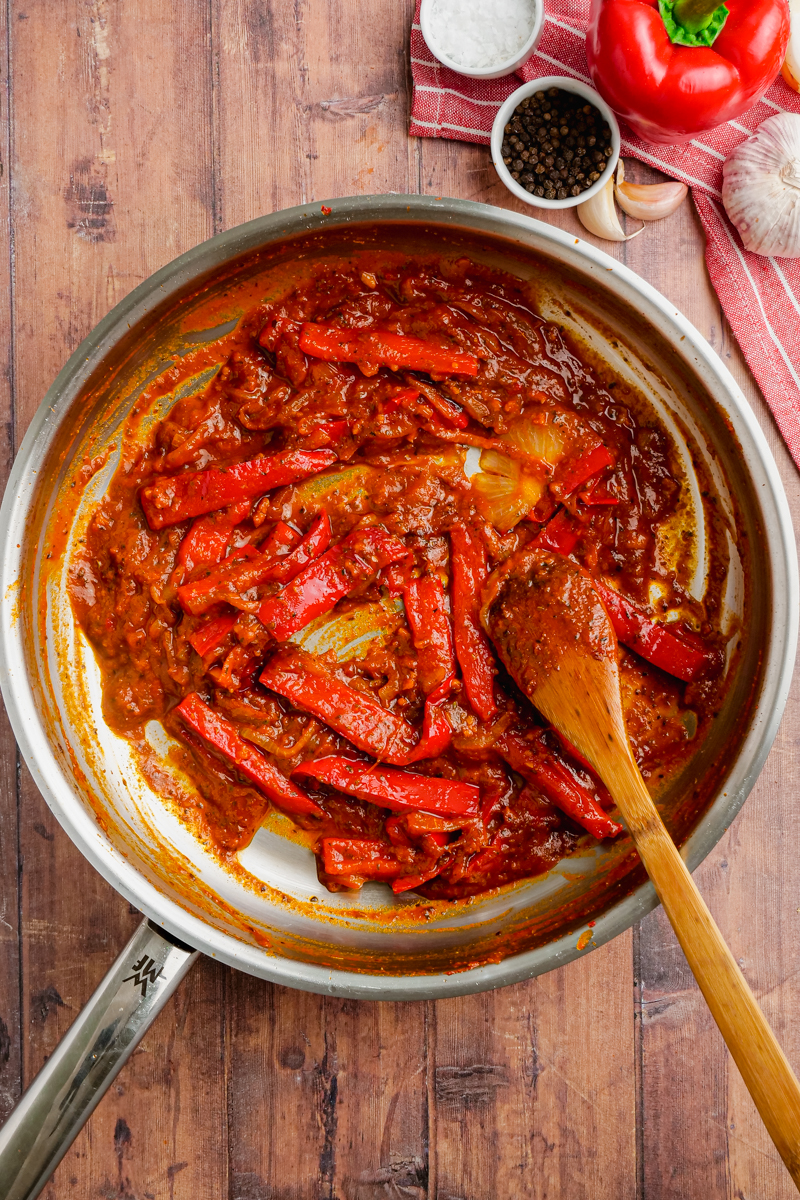 Stainless steel pan with peppers and onions in it, and a wooden spoon, cooking ropa vieja