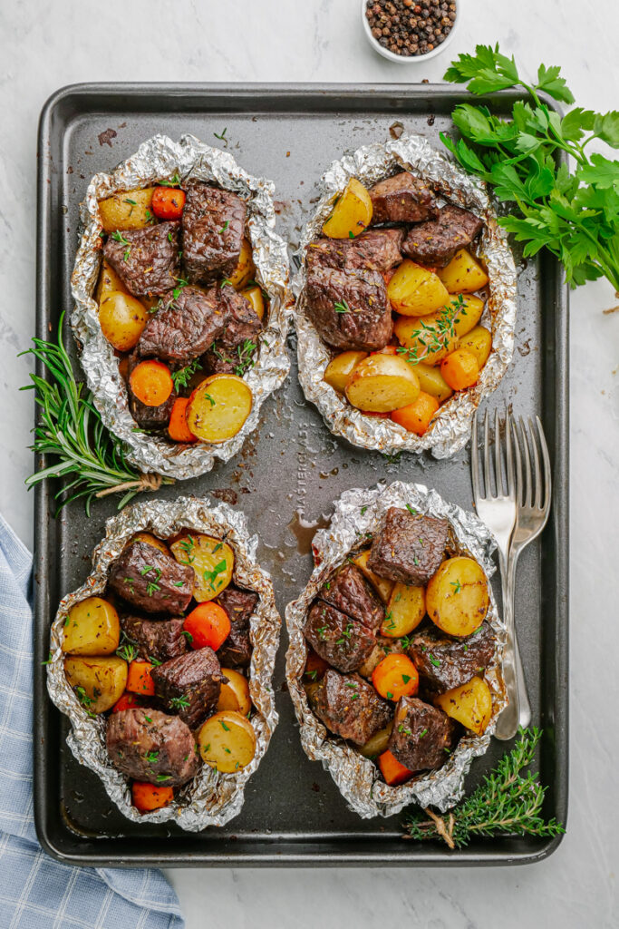 Steak and potato foil packs, 4 on a baking tray. 