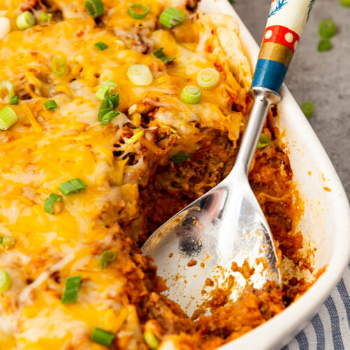 Enchilada casserole in a white casserole dish with a spoon in the corner