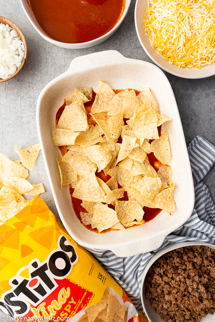 A white casserole dish with enchilada sauce and tortilla chips